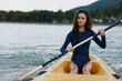 © SHOTPRIME STUDIO - Young female kayaker sits in a yellow kayak, paddling on calm water. She wears a dark wetsuit, focused expression, and moves with strength and balance through the current.