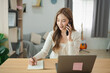 © WMSTUDIO - Young woman engages in phone call while taking notes at a modern workspace, showcasing multitasking and productivity in a contemporary home office setting.