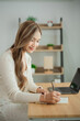 © WMSTUDIO - Young woman with long hair sitting at desk, writing in notebook, enjoying workspace, modern office environment, natural light, casual attire, focused expression