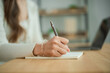 © WMSTUDIO - Woman Writing in Notebook with Pen While Sitting at Desk with Laptop in a Modern Office Setting During Daylight Hours