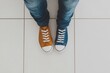 © Татьяна Евдокимова - Person standing on a tiled floor wearing jeans with one yellow and one blue sneaker, showing a unique personal style