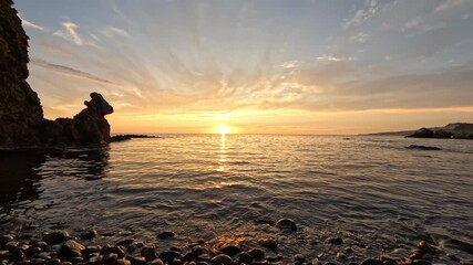Wall Mural - Sunset ocean beach. Golden light over calm sea and rocky shore creating a peaceful natural beauty scene