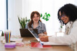 © Studio Marmellata - Two women collaborate at a desk with laptops and notebooks, one laughing while the other writes.