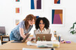 © Studio Marmellata - Two women collaborate on a project at a desk, one pointing at a laptop screen while the other smiles and types.