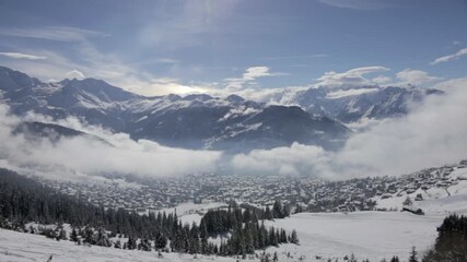 Wall Mural - Timelapse of snow-covered Swiss ski resort town Verbier blanketed in fog and clouds under crisp blue winter sky. Majestic mountain backdrop. Wide angle panorama, Switzerland.