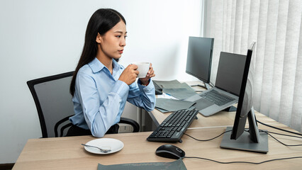 Female programmer holding coffee cup to drinking hot coffee during looking on laptop screen to reading database code