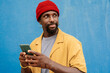 © VISTA by Westend61 - Man in red beanie with smartphone against blue wall looking away