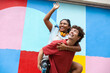 © VISTA by Westend61 - Joyful friends outdoors in playful piggyback ride by colorful wall