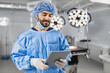 © sofiko14 - A surgeon in sterile attire reviews a tablet in a modern operating room, with surgical lights and equipment in the background.