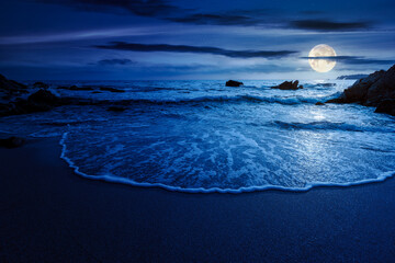 Wall Mural - calm sea landscape with wave rolling on sandy beach with boulders at night. scenic seascape in full moon light. relax and summer vacation on the shore concept