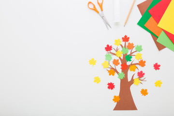 Wall Mural - Created tree with colorful maple leaves from application paper, glue stick, scissors on light gray table background. Making autumn decoration. Child handcraft. Empty place for text. Top down view.