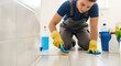 © Ksenia Pestereva - Floor cleaning in bathroom with worker scrubbing tiles and drain. Floor cleaning is important, and this sanitation worker in gloves applies cleaner with a brush.