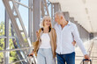 © Anastasiya - Joyful senior couple looking at each other, holding luggage, walking in airport