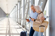 © Anastasiya - Senior travelers couple checking smartphone at airport corridor while waiting flight