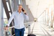 © Anastasiya - Mature man talking on smartphone at airport corridor while standing with suitcase