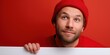 © Iryna - Young caucasian male in red beanie holding blank sign on vibrant red background