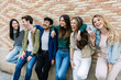 © Xavier Lorenzo - Young group of student people leaning against a brick wall, hugging each other and smiling. Youth community and friendship concept