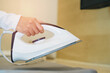© JK_kyoto - Close-Up of Hand Holding Modern Iron Over Fabric Ready for Pressing and Steam Treatment in Domestic Environment