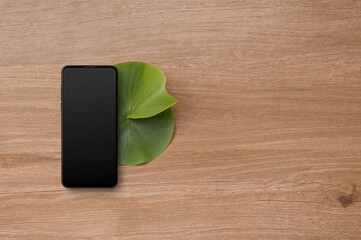 Wall Mural - Mobile device resting on a wooden surface beside a green lotus leaf with space for text