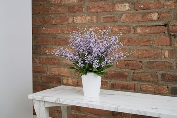Wall Mural - Beautiful artificial plant in a container on a marble surface near a brick backdrop, empty space for writing.
