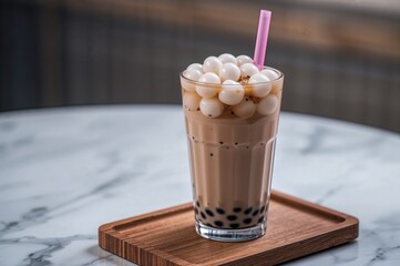 Wall Mural - Close-up of a glass filled with bubble milk tea featuring tapioca pearls, placed on a wooden tray atop a white marble surface with a straw, leaving room for text.