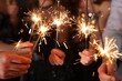 © New Africa - Friends celebrating New Year with sparklers and wine glasses indoors, closeup