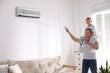 © New Africa - Father and son at home. Man switching on air conditioner with remote control