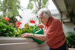 © Halfpoint - Elderly woman watering potted flowers on balcony.