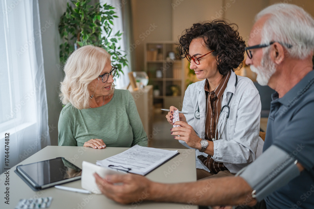 mature female doctor recommends medicines to patients during home visit ...