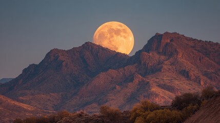 Wall Mural - A large bright moon rises above the jagged mountain peaks during dusk. The sky is painted in soft hues as the landscape appears tranquil and majestic inviting peace.