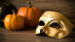 © freedarts - Close-up of golden Venetian-style carnival mask resting on wooden surface next to blurred pumpkins in background.
