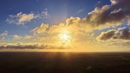 Wall Mural - A golden sunrise or sunset lights the sky with clouds passing over a dark, flat landscape.