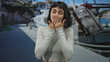 © Krakenimages.com - Young hispanic woman covers mouth with hand in front of building on a boat dock at a seaside port; flirty farewell.