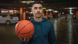 © Krakenimages.com - Young hispanic man holding a basketball in an indoor parking area, making a hand gesture as if calling someone to come over.