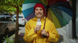 © Krakenimages.com - Man holding a microphone and colorful umbrella in a park setting, wearing a yellow raincoat, capturing a report in an urban environment on a rainy day.