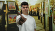 © Krakenimages.com - Young man in white shirt gesturing no with finger in art gallery surrounded by colorful paintings indoors with a serious expression on his face.