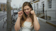 © Krakenimages.com - Young caucasian woman mimes crying tears with fingers on urban street sidewalk near bicycles and row houses; sarcasm.