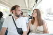 © Masakazu Tokashiki - A man and a woman are sitting on a bus. The man is wearing a white shirt and a black backpack. The woman is wearing a white dress and a handbag