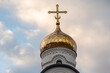 © denklim - Golden dome of church with cross against background of sky with clouds.
