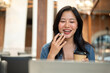 © bongkarn - Asian woman talking with holding pen and coffee in front of a laptop aside notebook on table in cafe