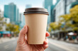 © aboutnuylove - Closeup of male hand holding disposable coffee cup on blurred city background