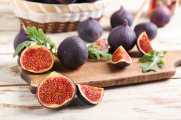 Wall Mural - Cutting board with fresh ripe figs and arugula leaves on white wooden background, closeup