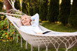 © New Africa - Senior woman with book resting in hammock outdoors