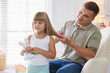 © New Africa - Father brushing his daughter's hair in armchair at home