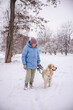 © StockMediaSeller - Elderly woman in a blue winter coat standing with her Golden Retriever on a snowy path. The woman holds the leash and looks at her dog while they enjoy the quiet beauty of the winter countryside.