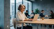 © Mauricio - Cheerful mature woman working on laptop in modern office with colleagues behind