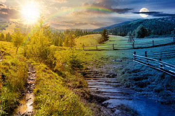Wall Mural - mountainous rural landscape in autumn. day and night time change concept. wooden fence near the path through grassy meadow on the hillside. scenery with fir forest on the mountains with sun and moon
