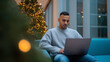 © Favio - Young hispanic man working on laptop in modern office with christmas tree lights in background.