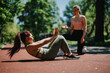 © qunica.com - Two women, one of European descent and one of Asian descent, exercising together outdoors in fitness wear, promoting teamwork, encouragement, and healthy lifestyle in a serene and sunny park area.