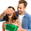 © vgstudio - Holiday sales, price discounts, celebrating ad concept - happy smiling man surprises laughing woman by covering her eyes while handing her green gift box. Isolated white background. Square image